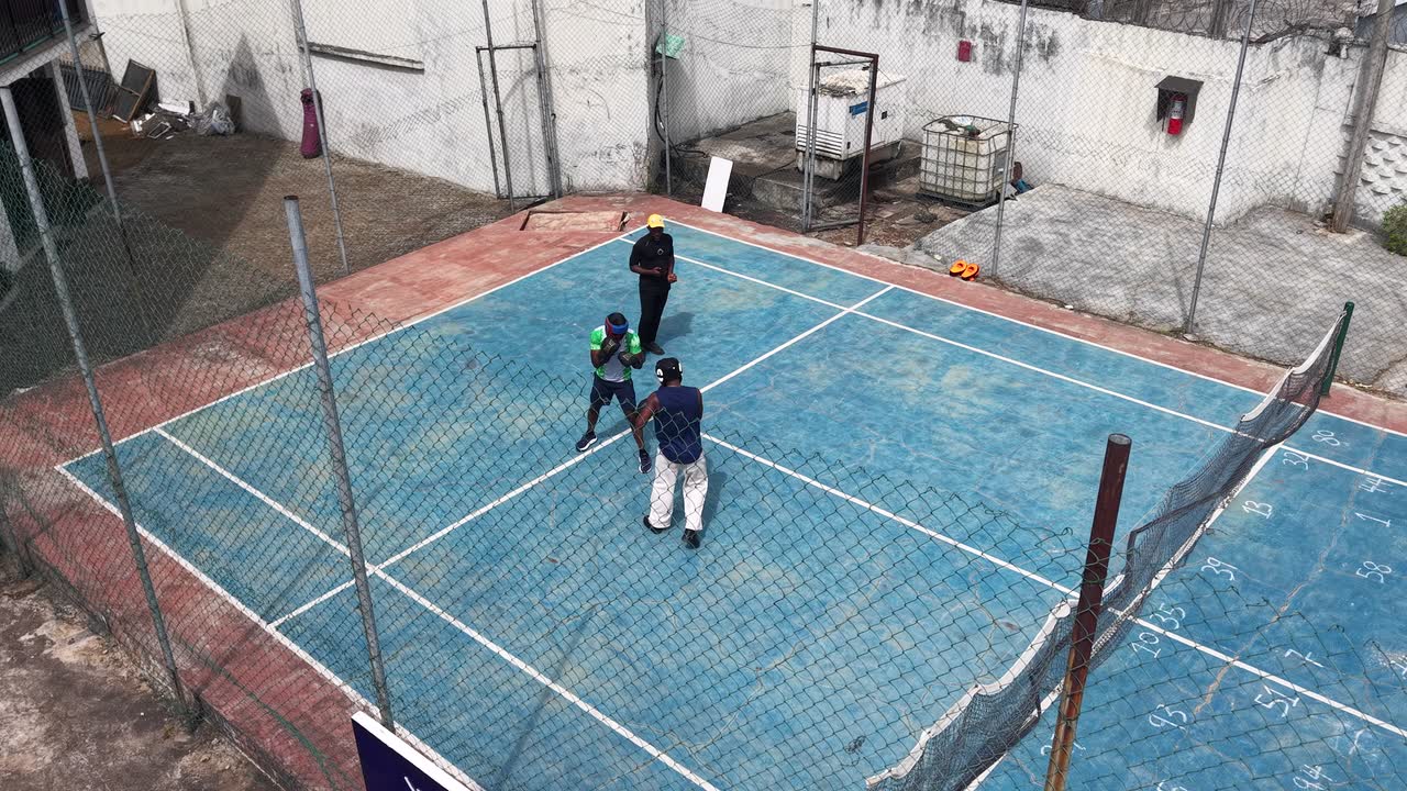 Drone view of two boxers sparring on the Glix outdoor court with a coach watching